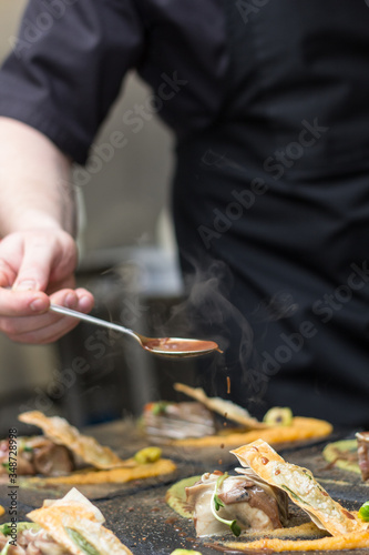 Chef in black outfit pouring sauce on food