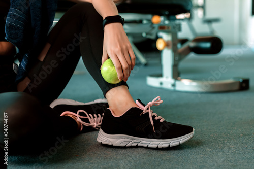 Woman exercise in gym fitness breaking and relax. hand holding apple fruit after training sport and dumbbell, water bottle on the ground.