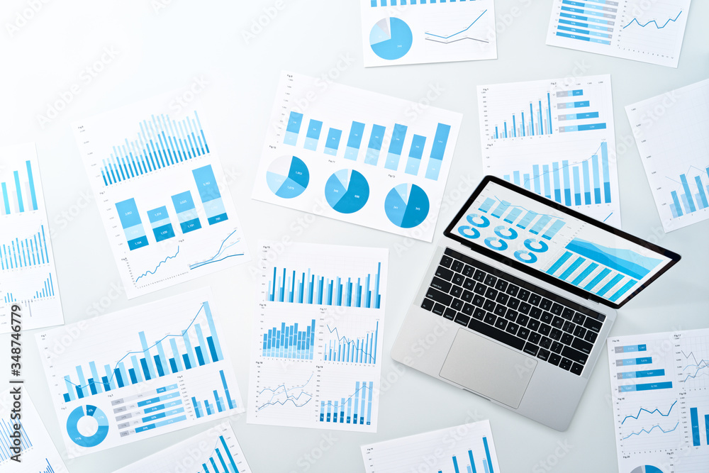 Business analysis and reports. Top view of reports amd laptop on white desk. Many blue graph and chart.