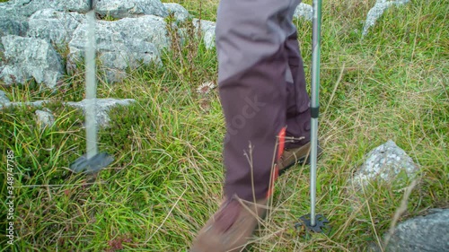 Adult Female And Male Legs Hiking Across Grassland With Trail Poles. High Angle, Slow Motion, Follow Shot photo