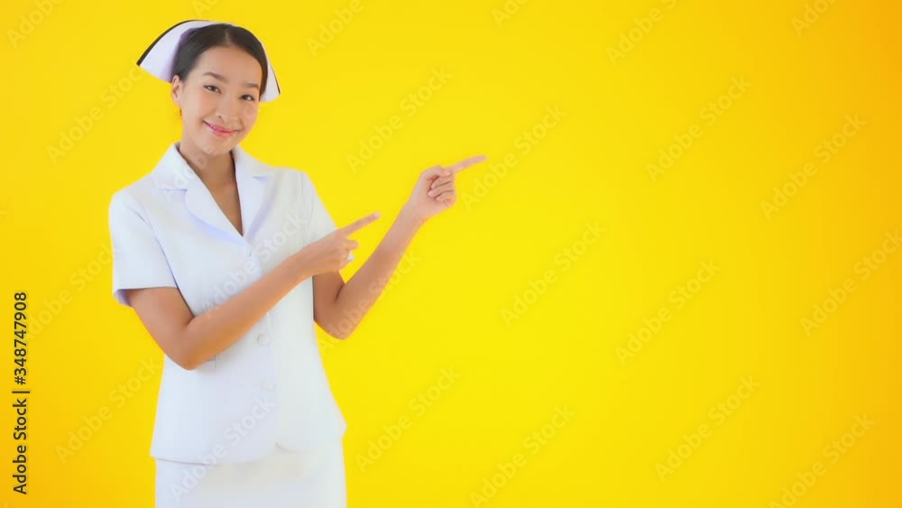 Thai Nurse in front of Yellow Background Pointing to Copy Space Static Thai Nurse in front of Yellow Background Pointing to Copy Space Static