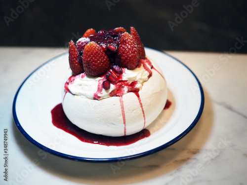 Summer Berry Pavlova  Meringue pavlova filled with fresh cream  fresh strawberry and pomegranate  served with juicy berry sauce on white plate. Selective focus.