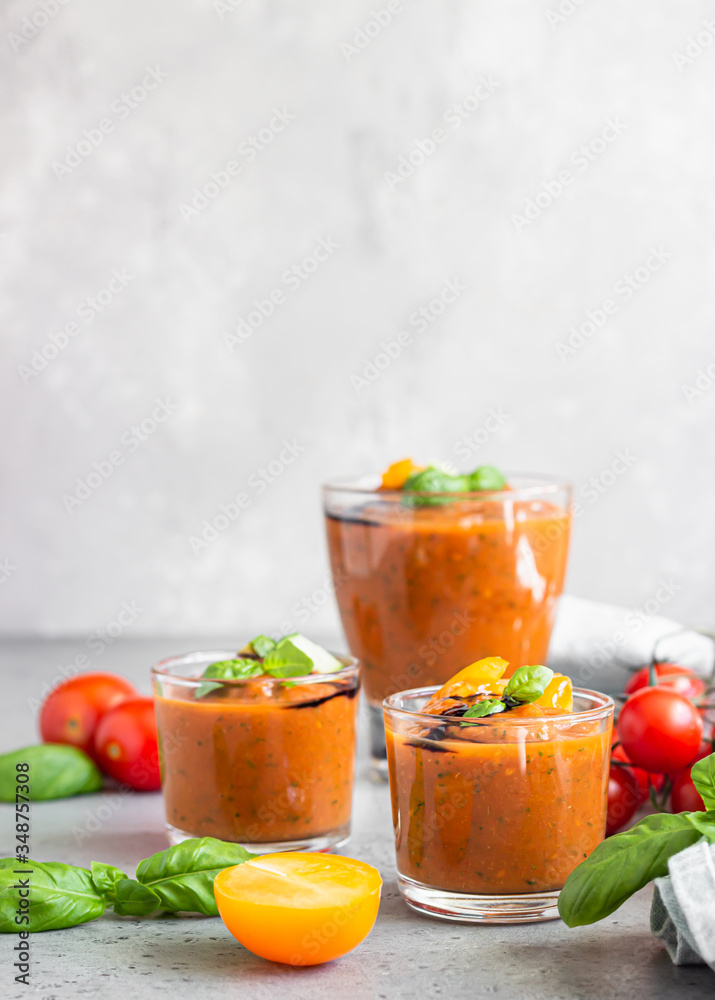Delicious gazpacho soup in glass. Traditional spanish cold soup puree gaspacho garnish with tomato, cucumber and basil. Grey concrete background. Delicious gazpacho soup in glass. Traditional spanish cold soup puree gaspacho garnish with tomato, cucumber and basil. Grey concrete background.