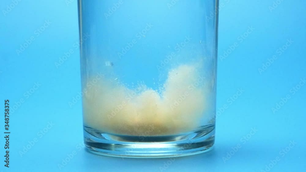 Close-up Pill antacid vitamin falling down in glass with bubbles orange effervescent on blue background. Close-up Pill antacid vitamin falling down in glass with bubbles orange effervescent on blue background.