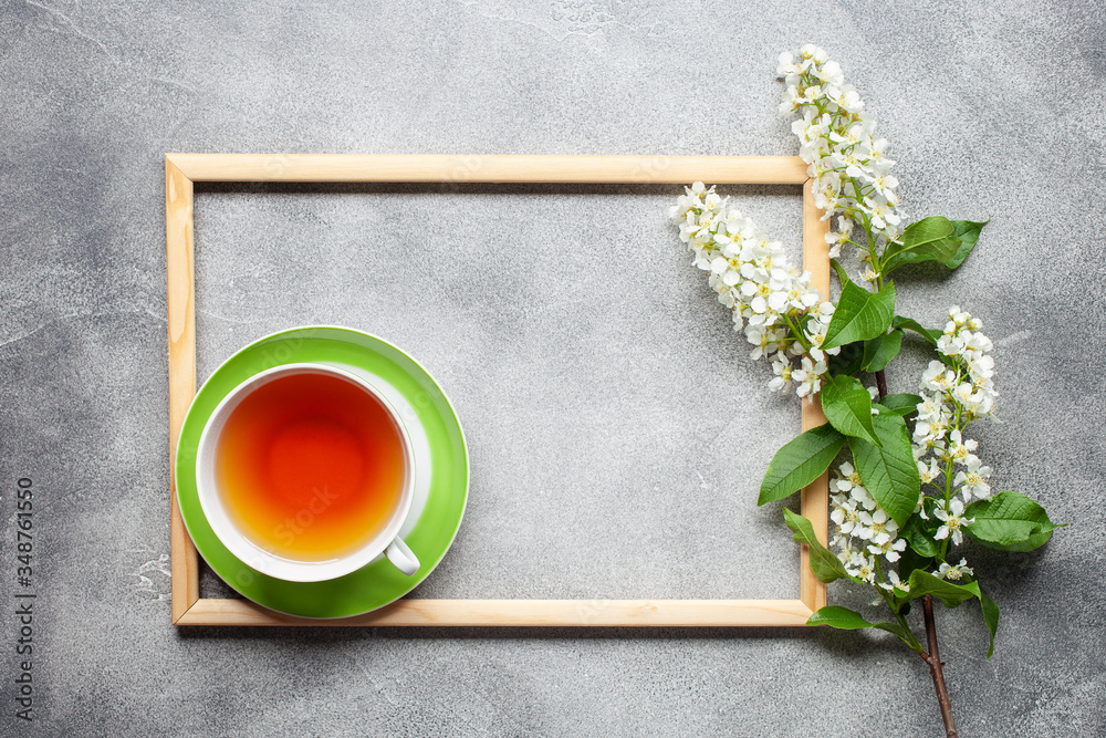 Cup of tea and a blossom branch of cherries on a picture frame on a grey background. Top view. Copy space Cup of tea and a blossom branch of cherries on a picture frame on a grey background. Top view. Copy space