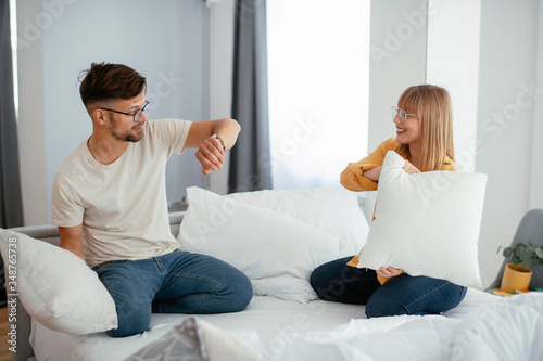 Young couple fighting pillows on the bed. Happy couple having fun at home. photo