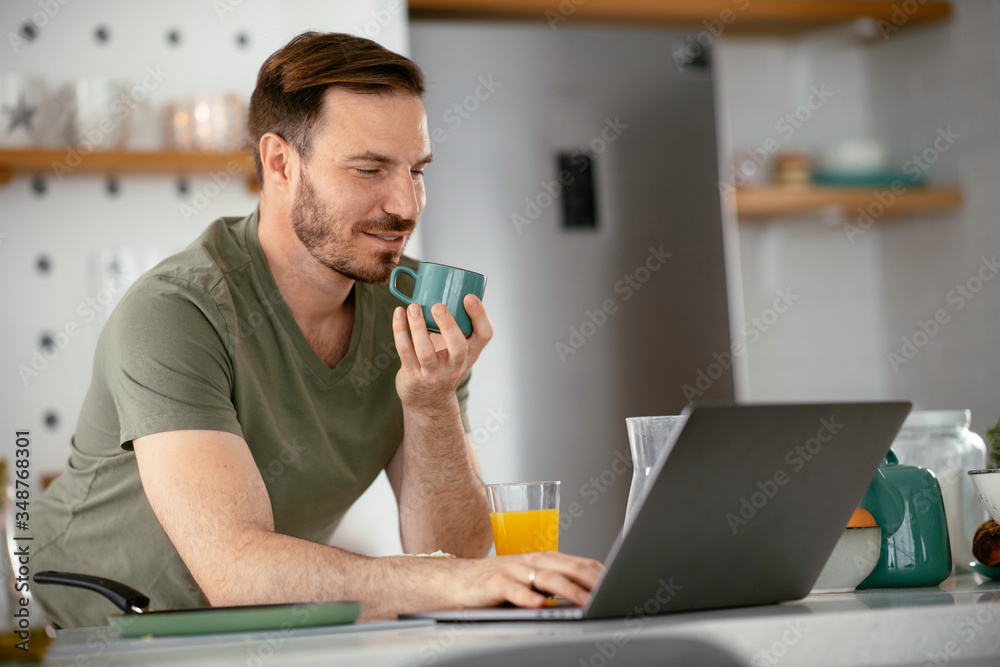 Handsome man drinking coffee in kitchen. Young man reading the news online. Handsome man drinking coffee in kitchen. Young man reading the news online.