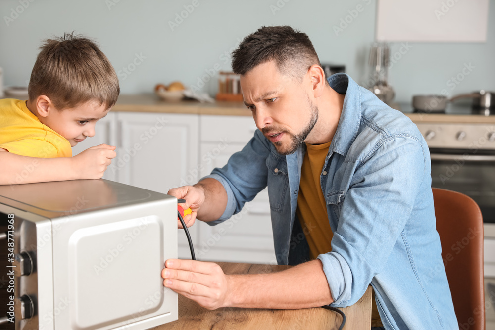 Obraz premium Little son helping his father to repair microwave oven in kitchen
