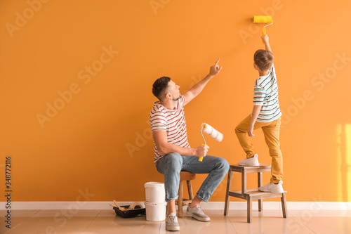 Fototapeta Naklejka Na Ścianę i Meble -  Little son helping his father to paint wall at home