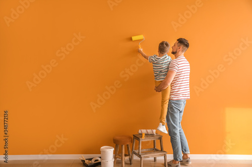 Little son helping his father to paint wall at home photo