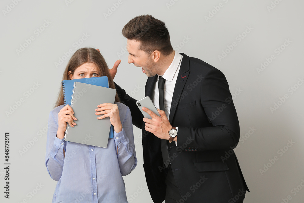 Angry boss scolding his secretary on light background Angry boss scolding his secretary on light background