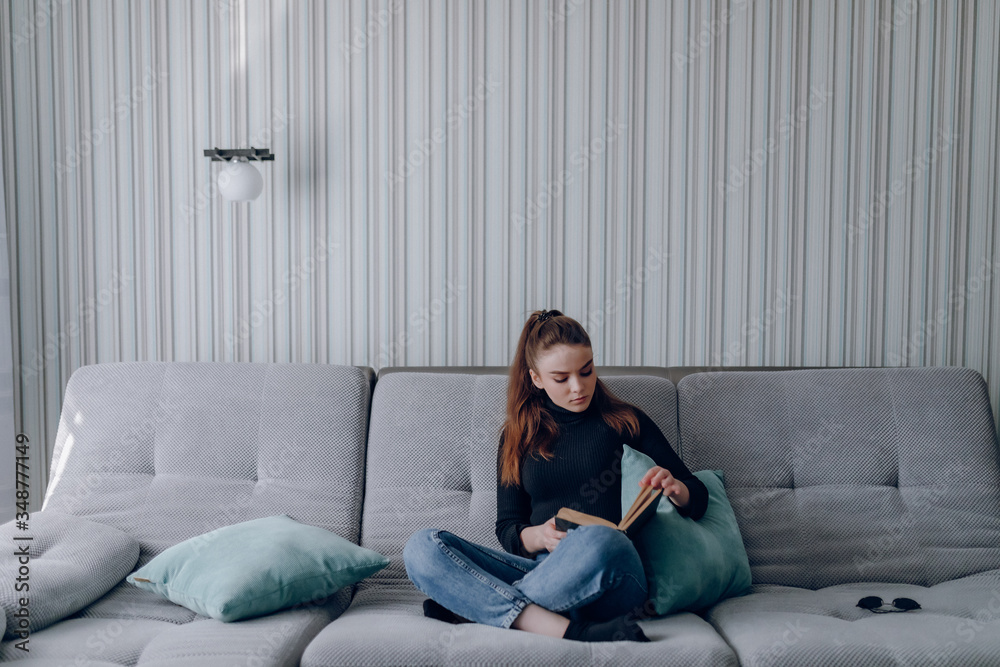 young attractive girl on the couch reads a paper book. mental development. useful use of time at home. home comfort. young attractive girl on the couch reads a paper book. mental development. useful use of time at home. home comfort.
