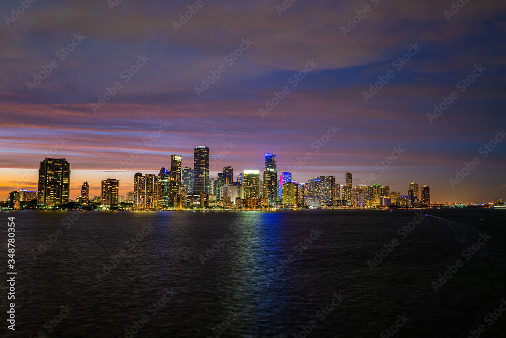 Miami city skyline panorama with urban skyscrapers over sea with reflection. Miami downtown view at night. Downtown Miami city center.