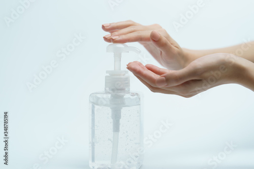 Hand with hand sanitizer in a clear pump bottle on a white background.
