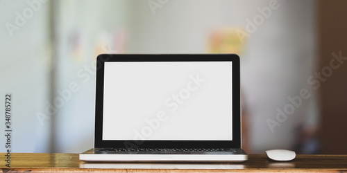 Laptop with wireless mouse putting on wooden counter bar for advertisement over comfortable sitting room as background.