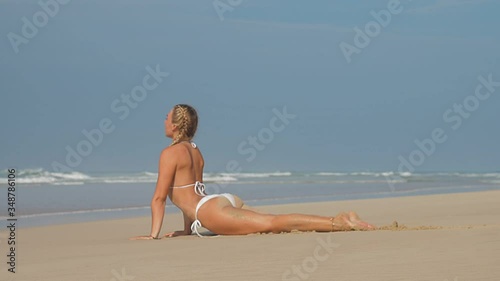 slim yoga coach practices breathing technique and lies in special cobra pose on golden beach sand closeup slow motion.Concept tropical beach yoga photo