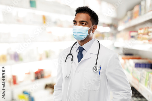 medicine, pharmaceutics and healthcare concept - indian male doctor or pharmacist with stethoscope wearing face protective medical mask for protection from virus disease over pharmacy on background