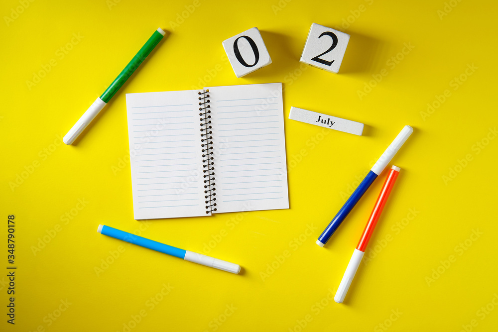 Date on the calendar July 2, notebook, felt-tip pens, on a yellow background