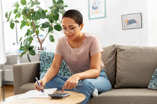 accounting, taxes and finances concept - young african american woman in glasses with papers and calculator at home photo