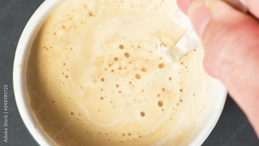 Stirring the foamy coffee with milk with a spoon as the camera zooms out. Stirring the foamy coffee with milk with a spoon as the camera zooms out.