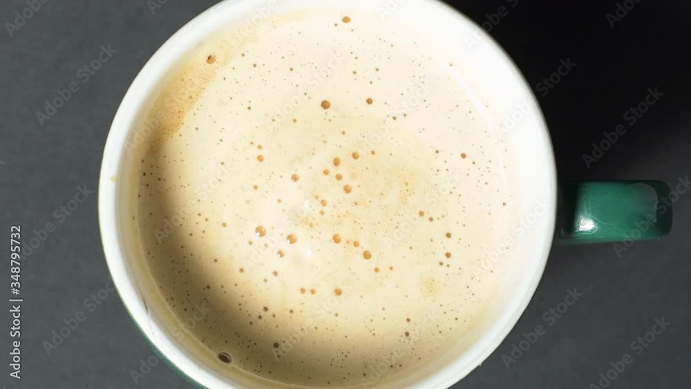 Frothy coffee with milk spinning in the mug as the camera zooms away. Camera zooms out from cup of coffe.