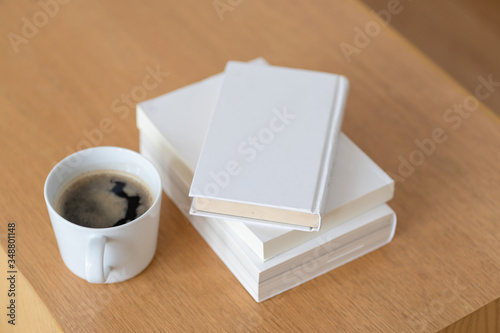 Cup of coffee with blank closed white book on wooden table for morning refreshment. Concept lifestyle comfortable working at home