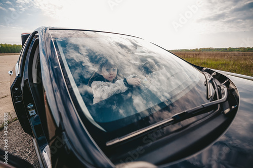 Cute baby girl sits inside the car and looks in the windshield on the beautiful sky. Closeup