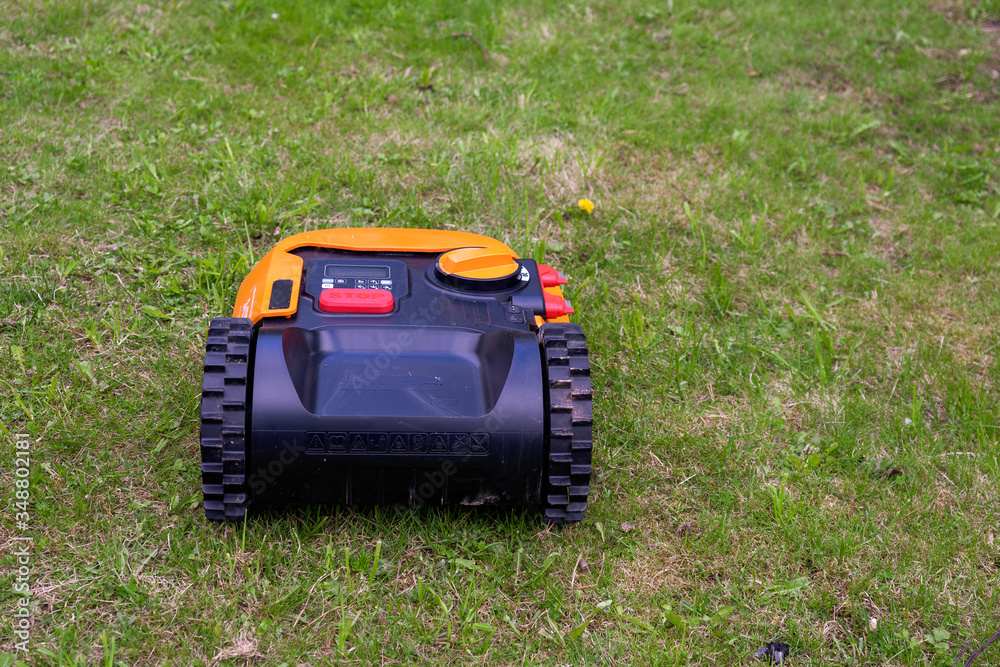 A robotic lawn mower (lawnmower) at work on a spring lawn. Back view A robotic lawn mower (lawnmower) at work on a spring lawn. Back view