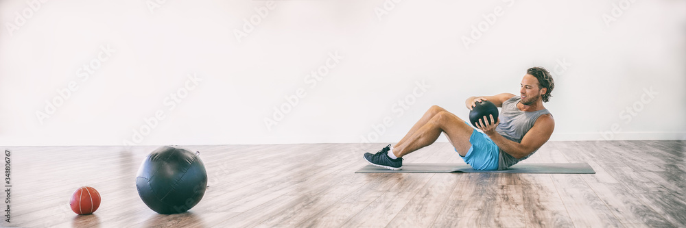 Fototapeta premium Ćwiczenia fitness w domowej siłowni brzuszki z piłką lekarską sprawny mężczyzna ćwiczący brzuszki z ważonymi rosyjskimi zwrotami akcji ćwiczenia trening panoramiczny baner.