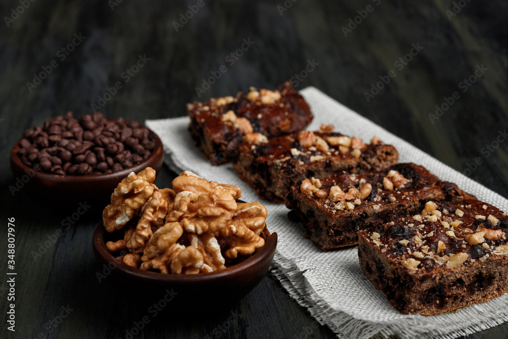 pieces of chocolate brownie and walnuts next to walnuts and chocolate in clay pots in the foreground pieces of chocolate brownie and walnuts next to walnuts and chocolate in clay pots in the foreground