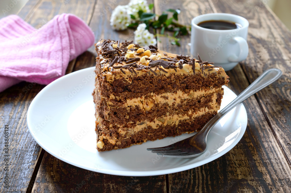 Chocolate cake with nut cream on a wooden table. A piece of cake on a plate and a cup of coffee. Chocolate cake with nut cream on a wooden table. A piece of cake on a plate and a cup of coffee.