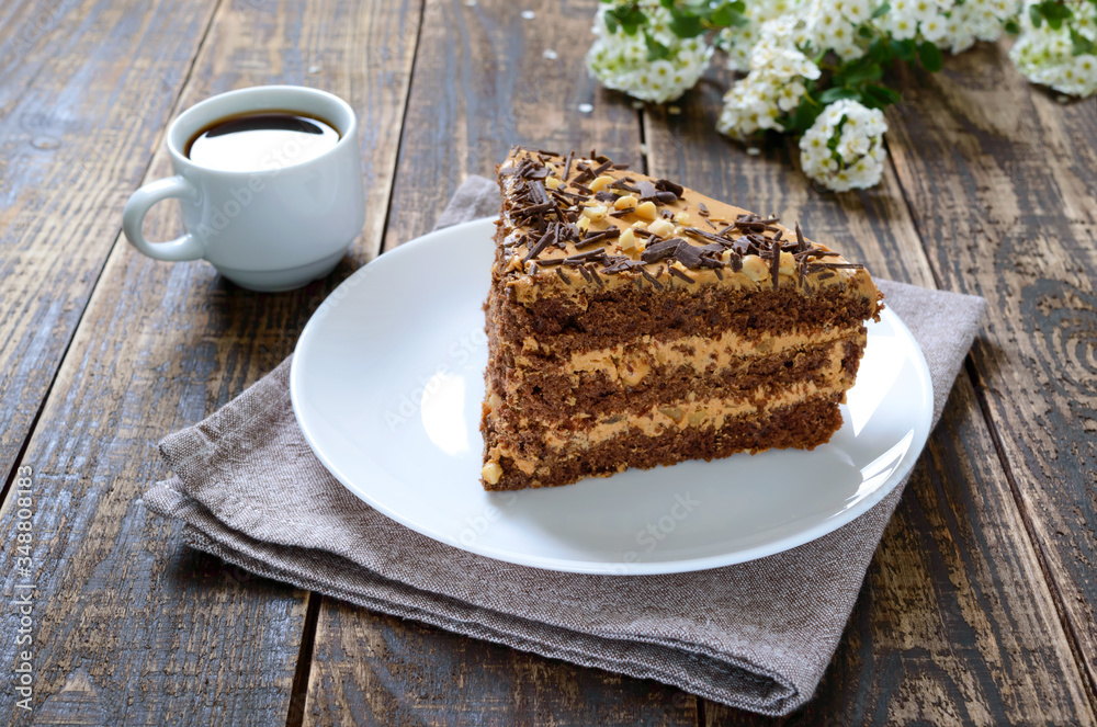 Chocolate cake with nut cream on a wooden table. A piece of cake on a plate and a cup of coffee. Chocolate cake with nut cream on a wooden table. A piece of cake on a plate and a cup of coffee.