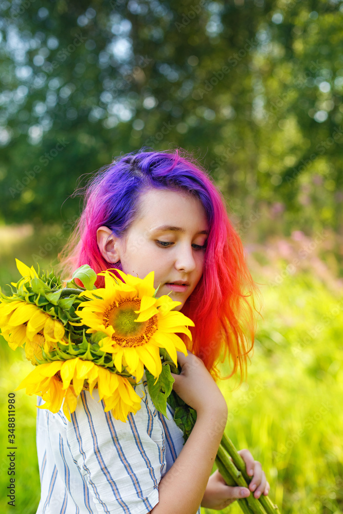 Pink and lilac strands of hair. A beautiful happy teenage girl with a sunflower enjoys nature and laughs on a summer field. The sun's glare, the sun's rays, the sun's radiance. Illuminated Pink and lilac strands of hair. A beautiful happy teenage girl with a sunflower enjoys nature and laughs on a summer field. The sun's glare, the sun's rays, the sun's radiance. Illuminated