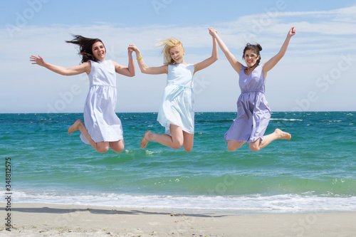 Three young laughing girls in same dresses are jumping near the sea