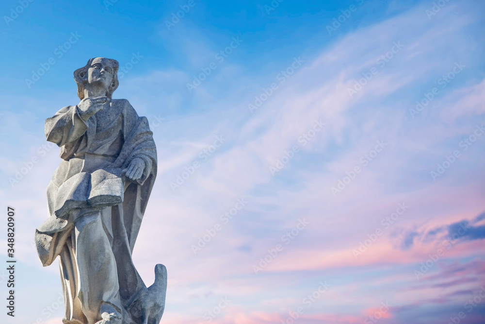 Obraz premium Ancient stone statue of St. John the Evangelist with eagle against blue sky.