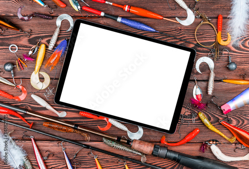 Fishing rod, tackles and fishing baits, reel on wooden board background with tablet computer isolated white screen. Empty space for text