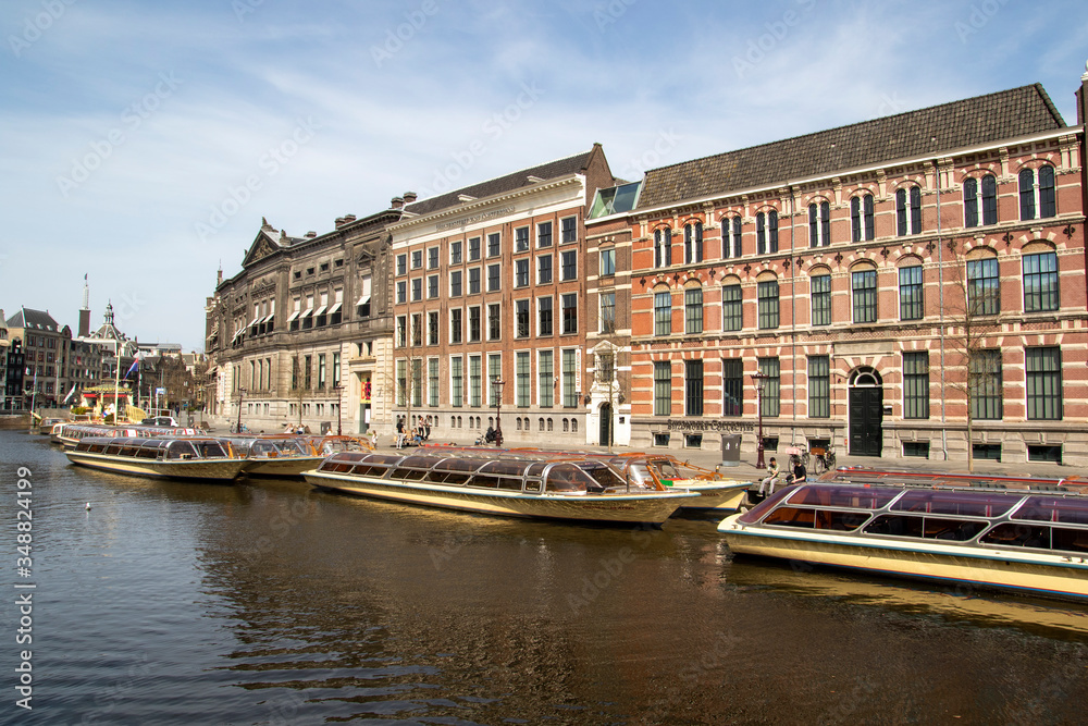 Naklejka premium Old historical buildings in Amsterdam. With therefore empty tour boats because they are not used by the world wide corona covid 19 crisis, so there are no tourists n