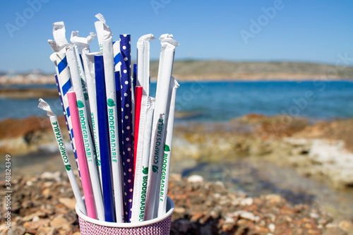 Paper drinking straws in paper cup outside on rocks next to sea