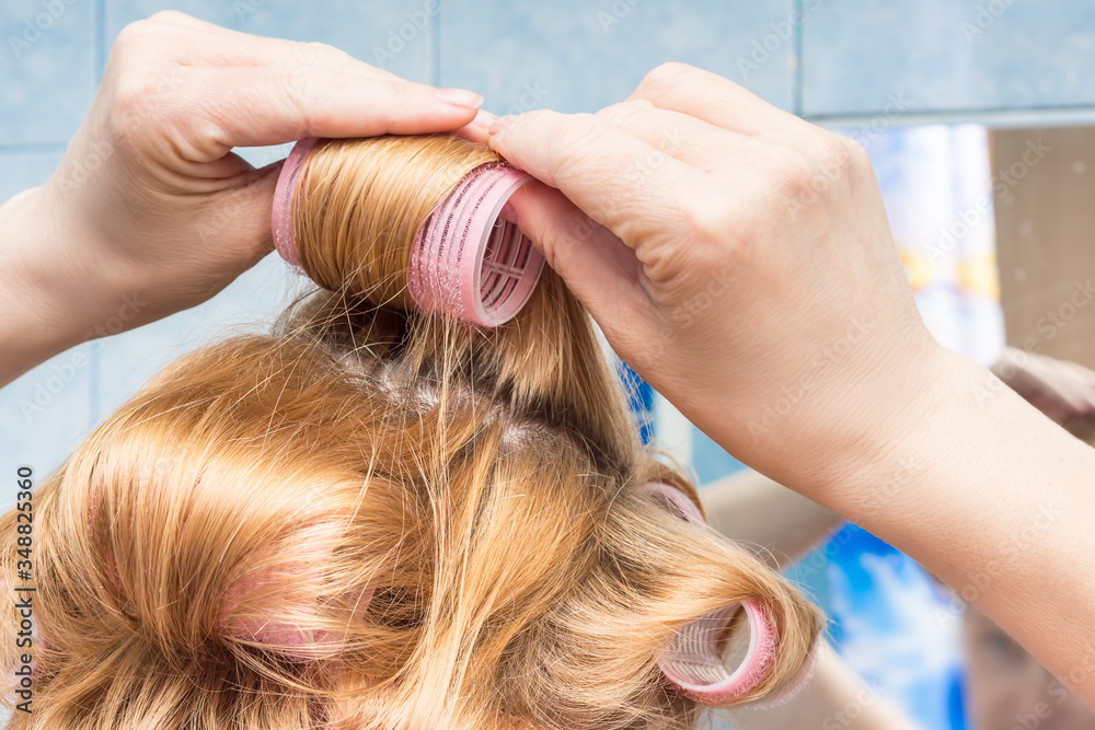 Fototapeta premium A middle-aged woman of European appearance winds curlers on her hair at home in the bathroom.