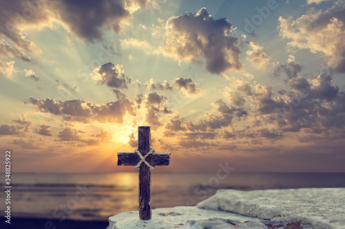 Wooden Christian cross on rocks against beautiful golden sunrise above the sea