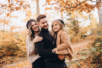 Stylish family in the autumn forest. Models. A young guy and a girl stand on a forest road among yellow leaves and hold their daughter in their arms.