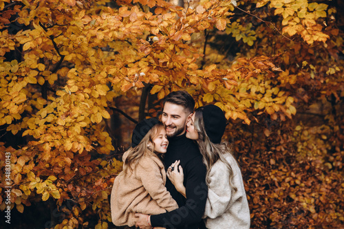 Stylish family in the autumn forest. Models. A young guy and a girl stand on a forest road among yellow leaves and hold their daughter in their arms.