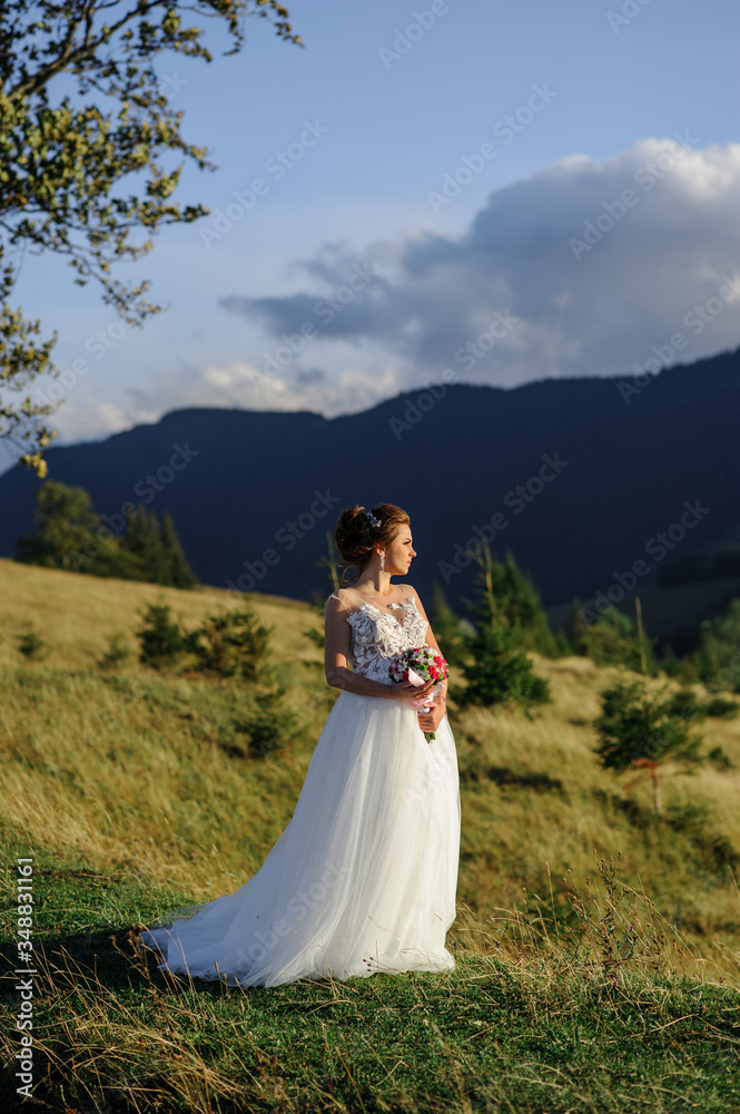 The bride herself with a wedding bouquet poses against the backdrop of the mountains at sunset.