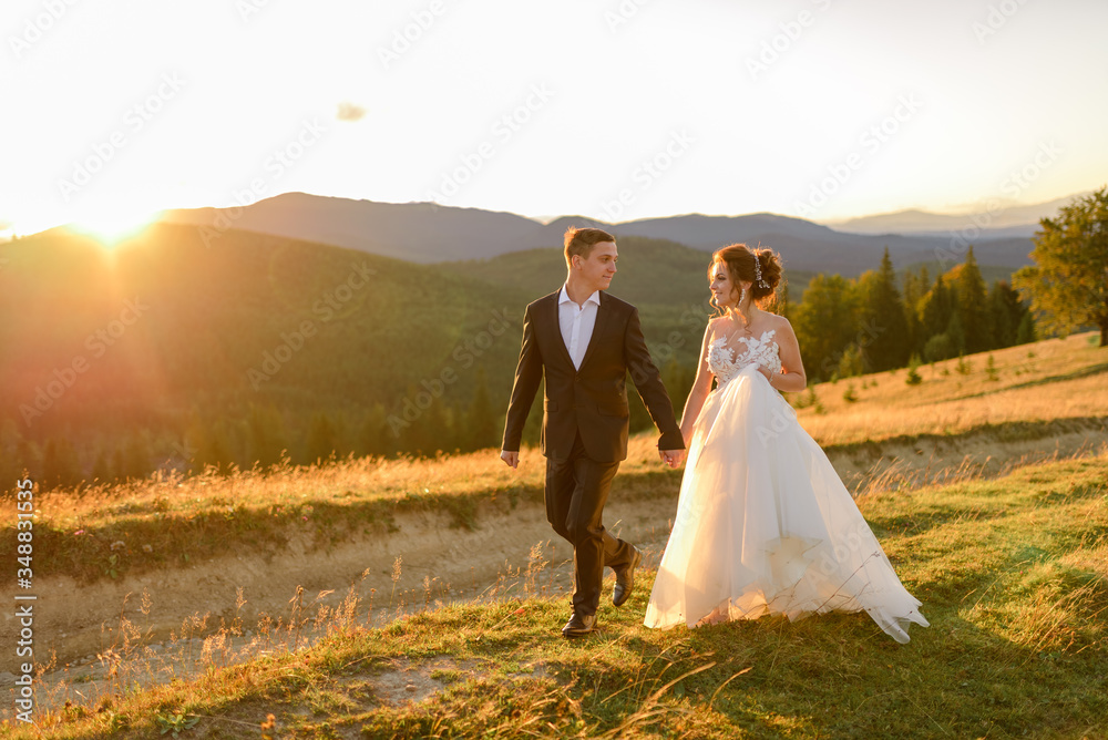 Wedding photography in the mountains. The bride and groom hold hand and walk at sunset.