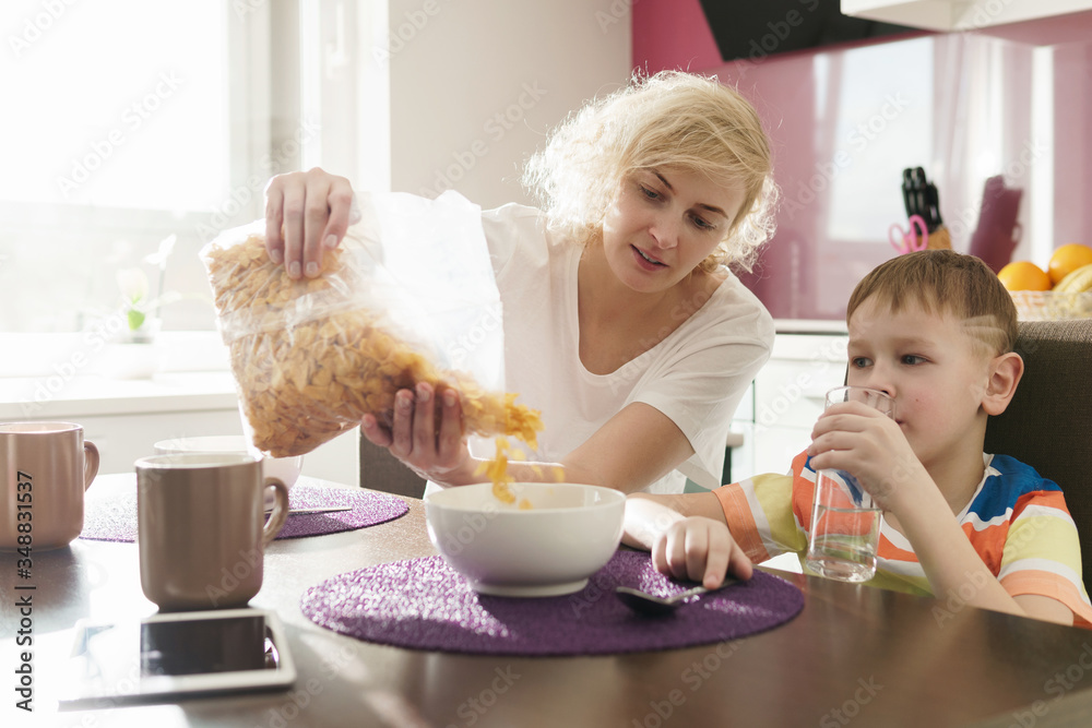 Beautiful mother and her cute son eating cornflakes for breakfast