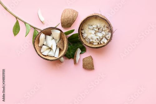 Coconut cut into pieces, coconut shavings, a branch of green leaves lies on a pink background. View from above. Place for text. Flat lay