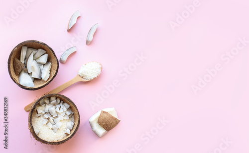Coconut cut into pieces, coconut shavings, a branch of green leaves lies on a pink background. View from above. Place for text. Flat lay