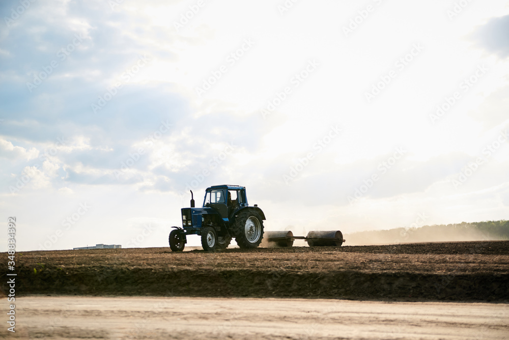 Agricultural work on field with black soil. Blue tractor riding and seeding countryside. Rural works in spring. Environmental protection concept. Ecological products cultivation. Natural background. Agricultural work on field with black soil. Blue tractor riding and seeding countryside. Rural works in spring. Environmental protection concept. Ecological products cultivation. Natural background.