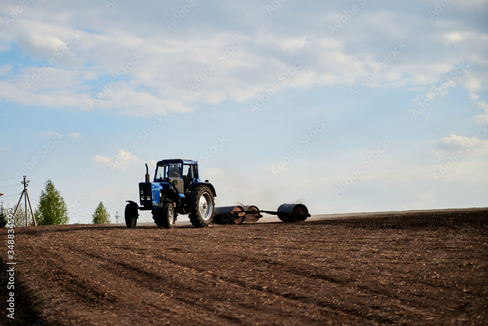 Fototapeta premium Agricultural work on field with black soil. Blue tractor riding and seeding countryside. Rural works in spring. Environmental protection concept. Ecological products cultivation. Natural background.