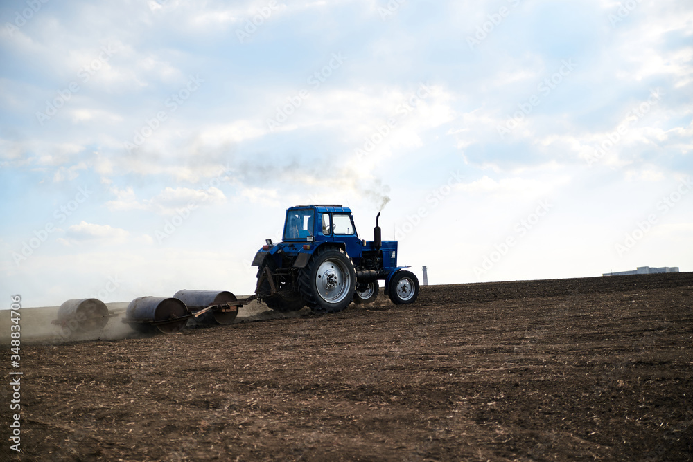Obraz premium Agricultural work on field with black soil. Blue tractor riding and seeding countryside. Rural works in spring. Environmental protection concept. Ecological products cultivation. Natural background.